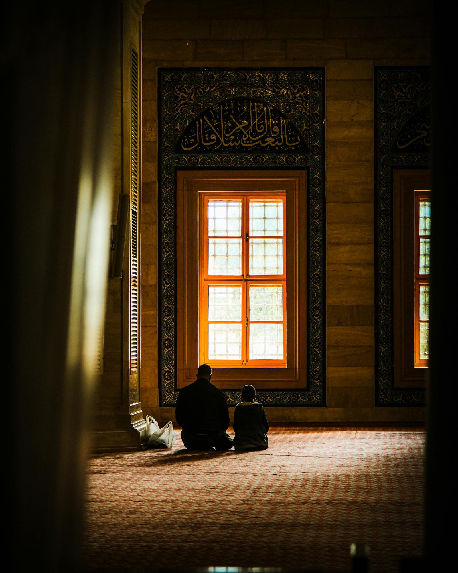 A father and child sit together in prayer inside a beautifully decorated mosque.